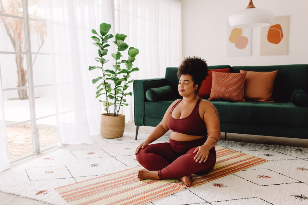 Body positive woman doing mindfulness workout at home. Beautiful female in sports wear practicing meditation at home