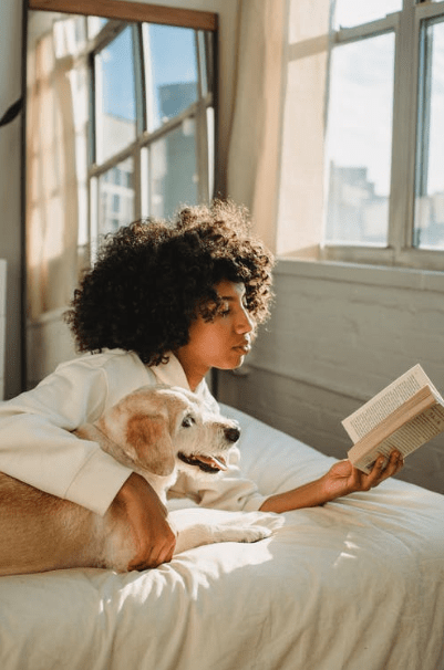 concentrated-young-black-woman-cuddling-curious-obedient-dog-while-reading-book-ob-bed